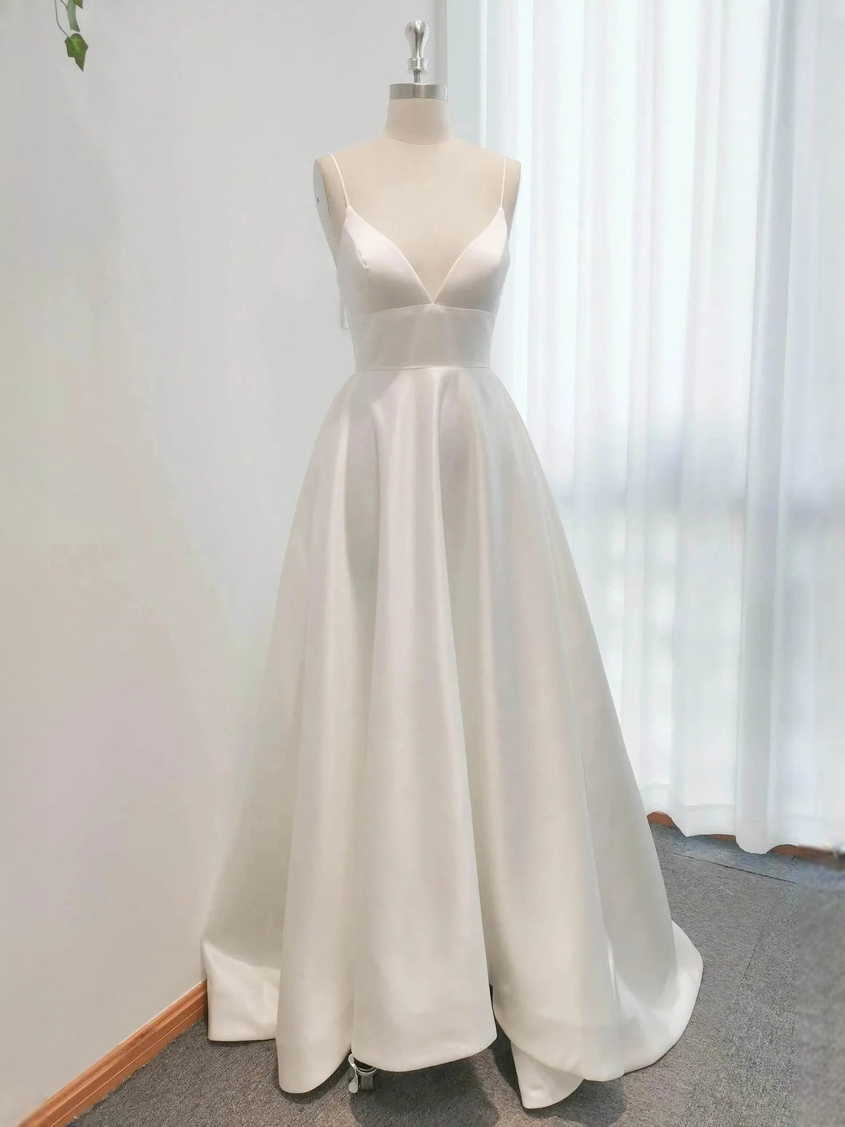 Ivory satin V-neck wedding dress on dress form, A-line skirt, floor-length