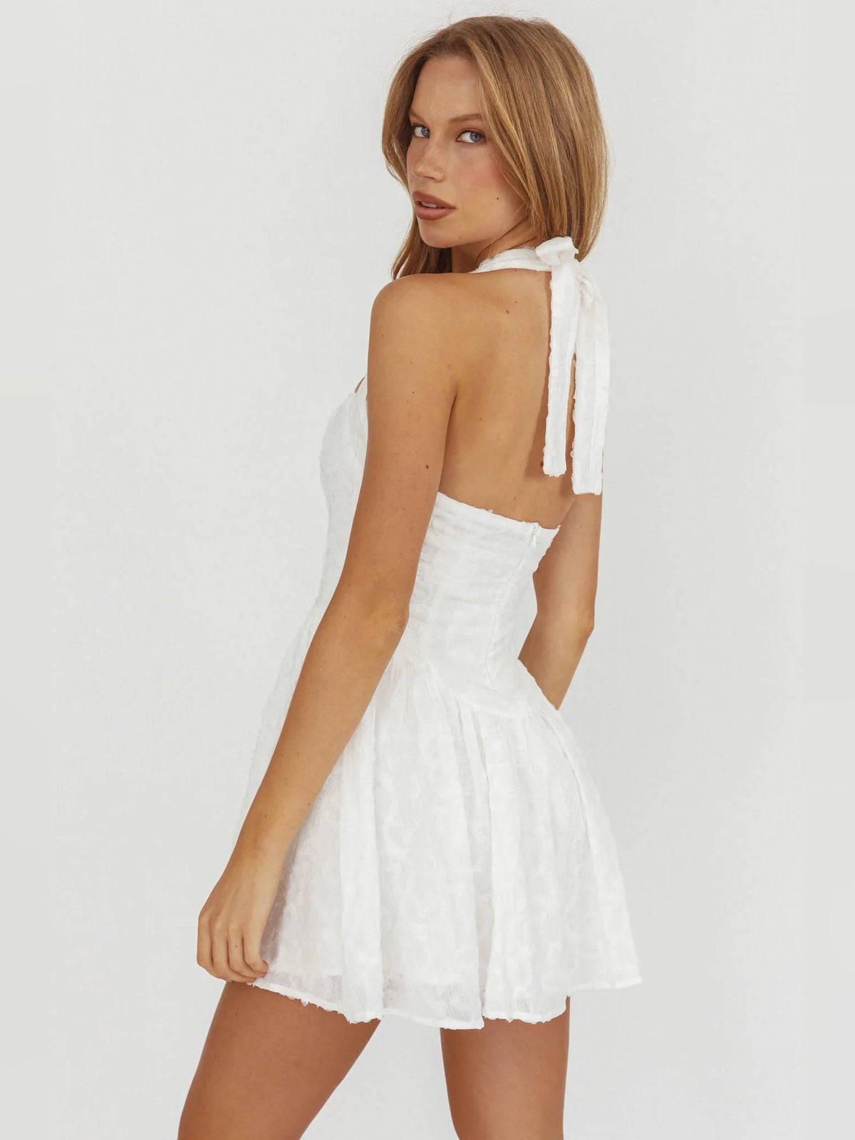 White halter mini dress with open back, bow tie at neck, textured tiered skirt