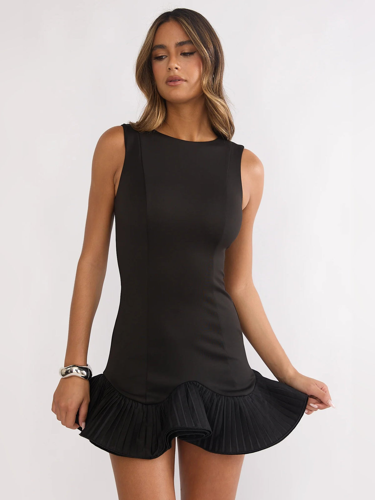 Black sleeveless mini dress with pleated ruffle hem and fitted waist.