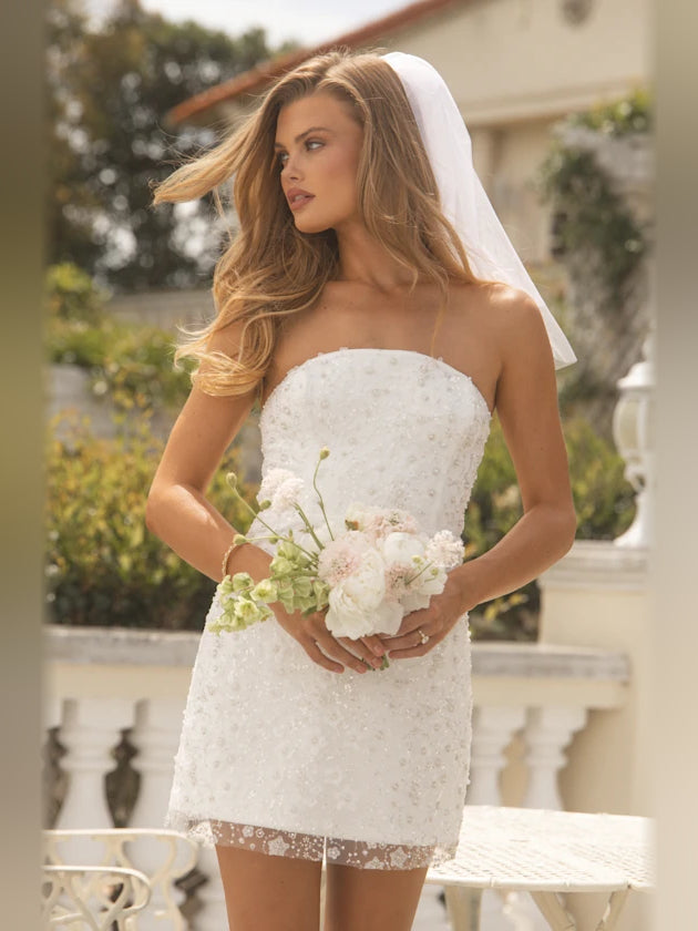 White strapless sequin mini dress with floral bouquet in hands, sweetheart bodice