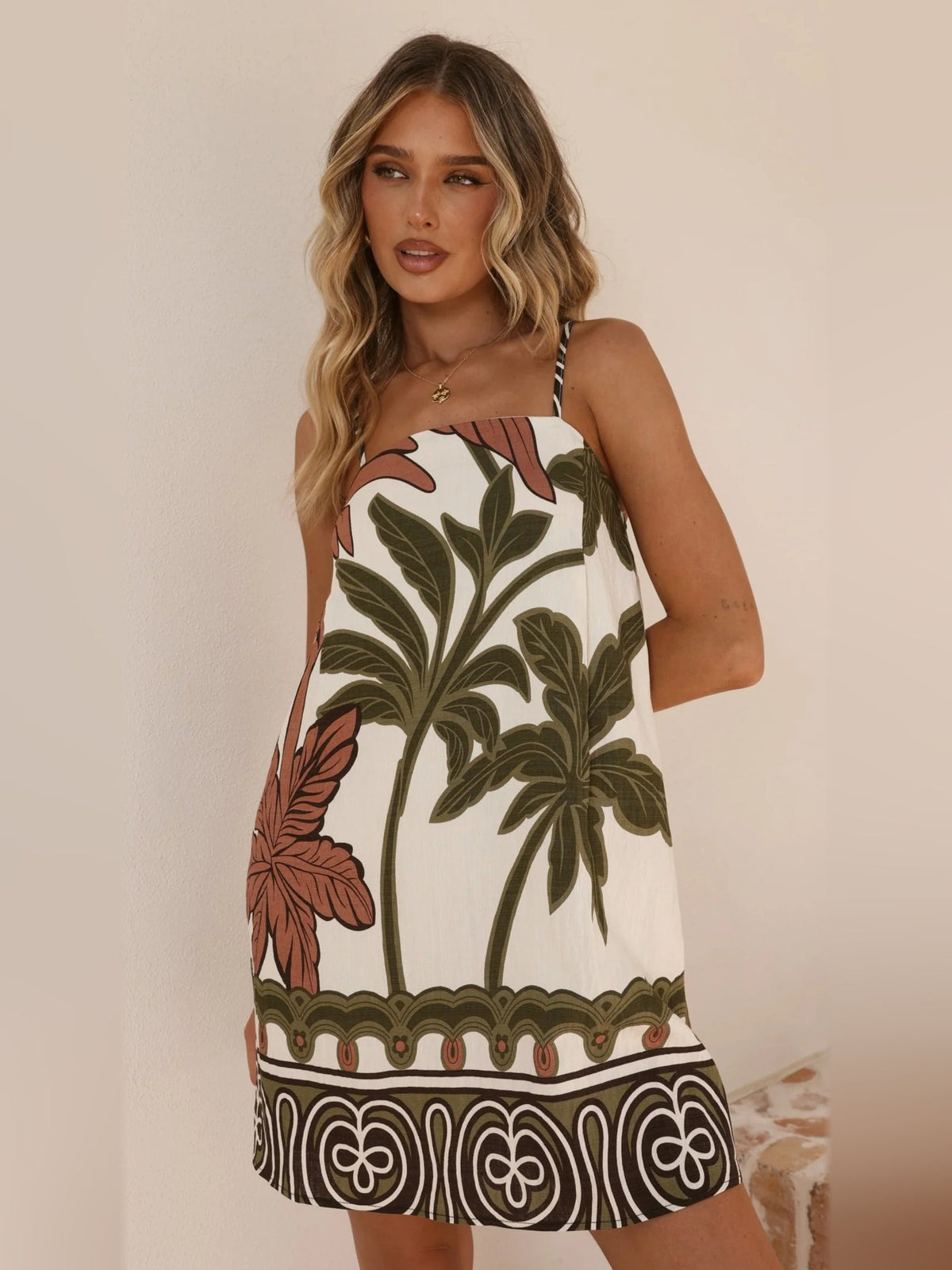 Beige mini sleeveless dress with spaghetti straps and large green leaf print