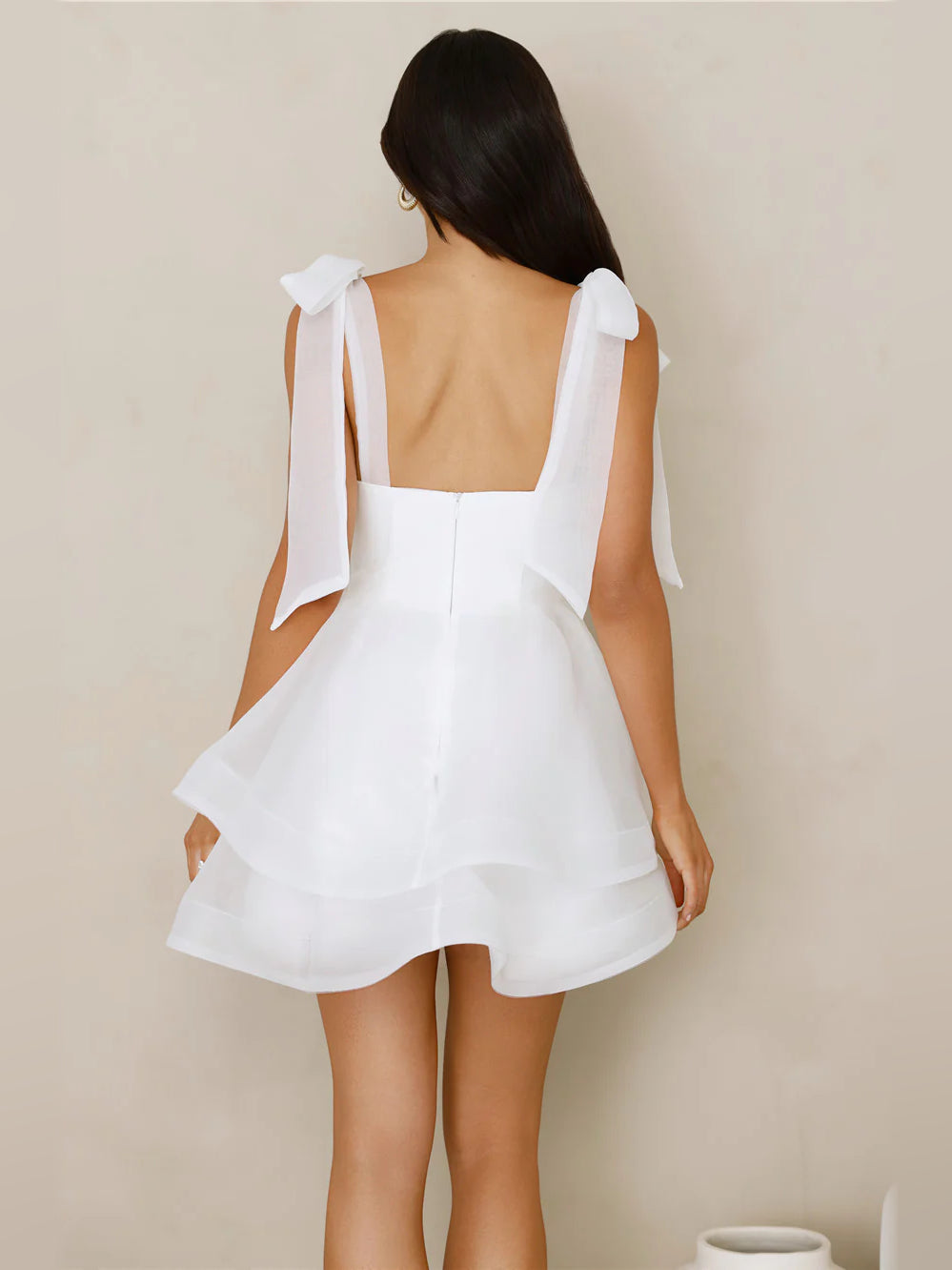 White mini dress with open back, bow-tied shoulder straps, layered ruffle skirt
