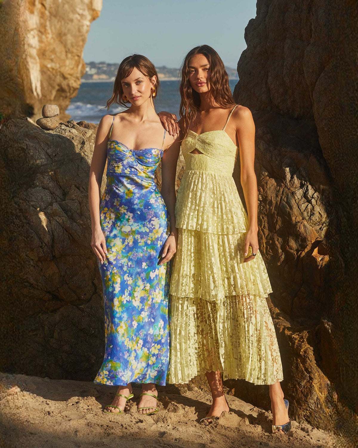 Light blue floral satin maxi dress on model beside gold tiered dress
