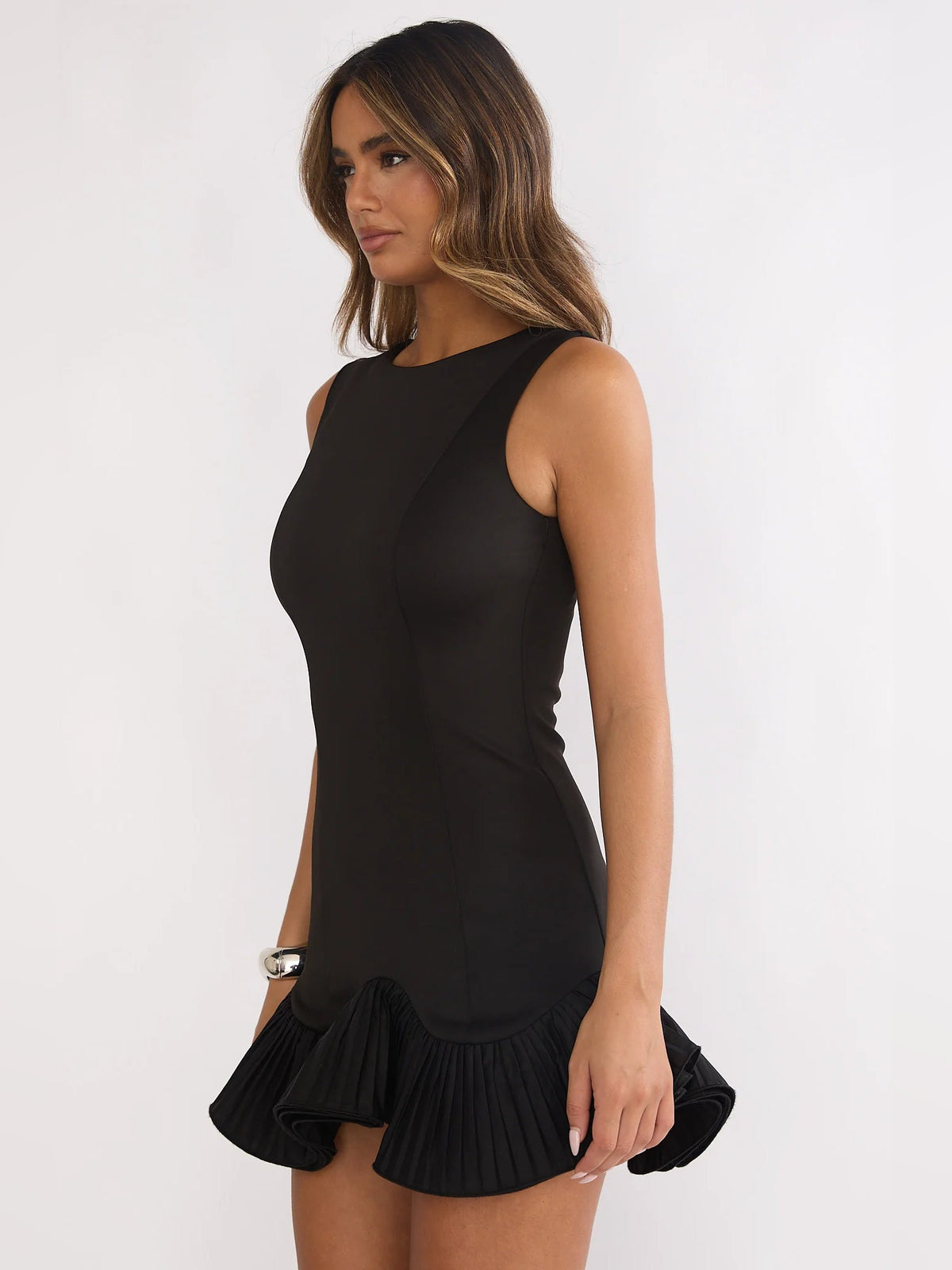 Black sleeveless mini dress with pleated ruffle hem, shown from back angle.