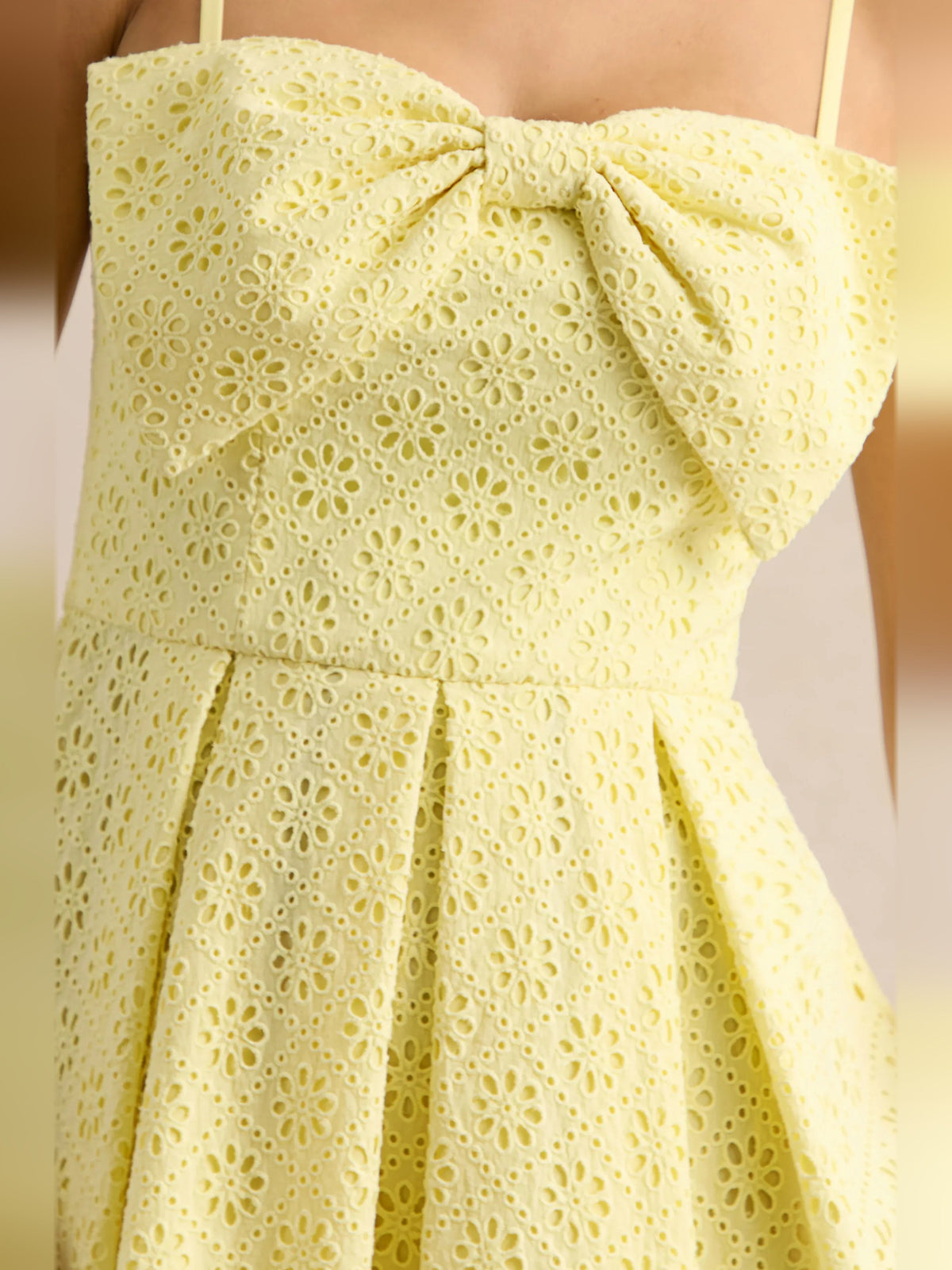 Lemon yellow eyelet dress close-up showing bow detail and pleated waist seam
