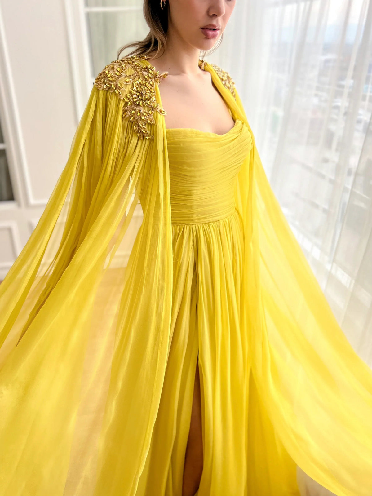 Yellow floor-length dress with ruched bodice, gold-embellished tulle cape, front slit