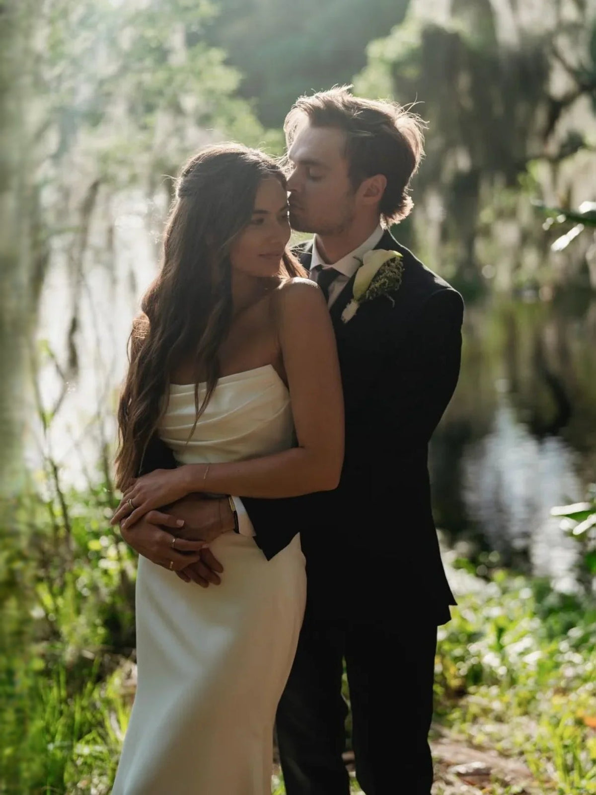 White strapless mermaid wedding dress, bride and groom embrace; fitted silhouette and train