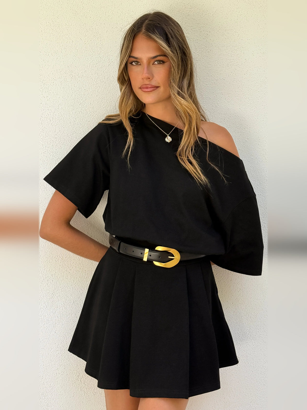 Black one-shoulder mini dress close-up with gold buckle belt and short draped sleeve