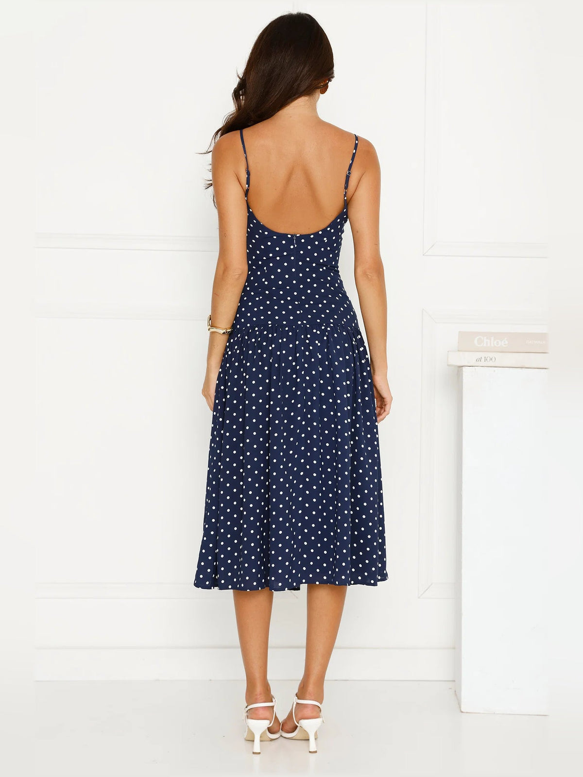 Back view of navy polka dot midi dress with open sleeveless back and flared hem