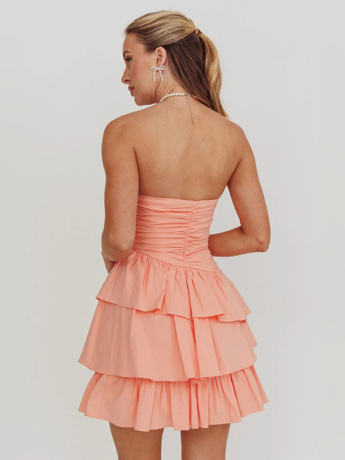 Back view of coral strapless mini dress with ruched bodice and tiered ruffles