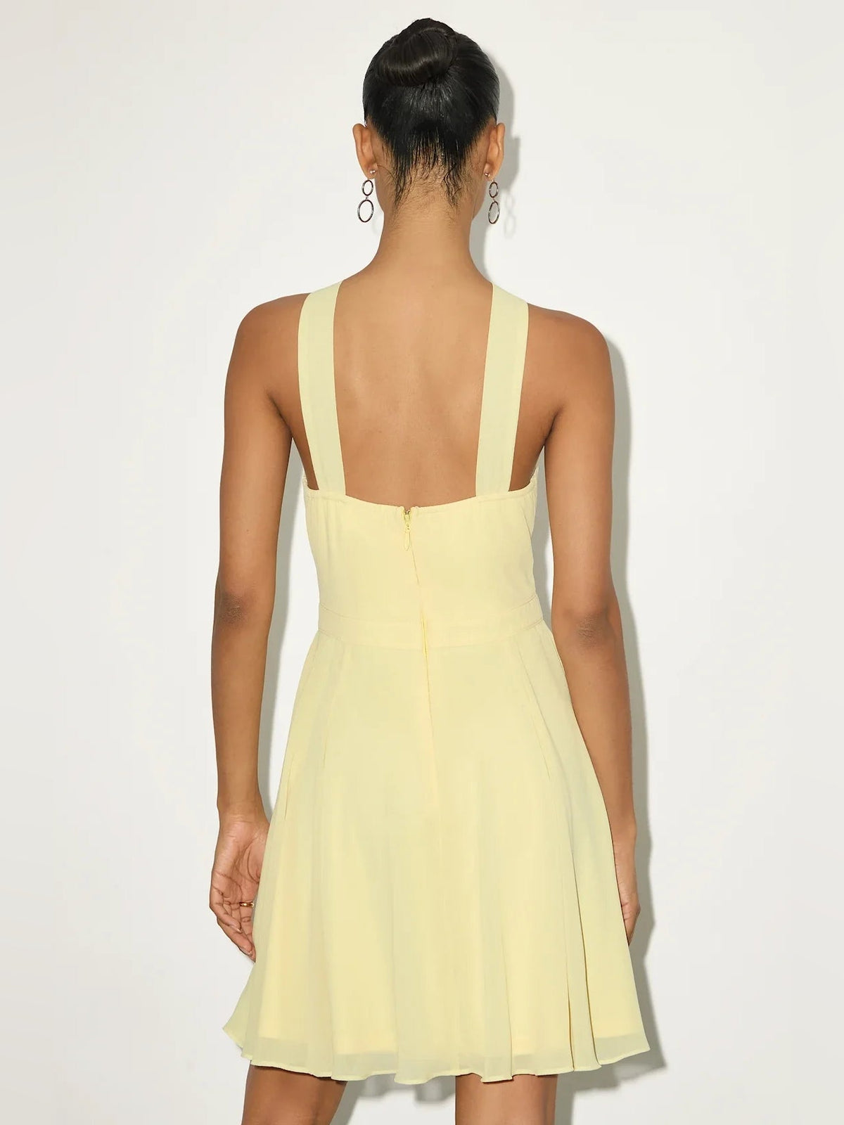 Back view of pale yellow halter mini dress with open back and soft pleated skirt