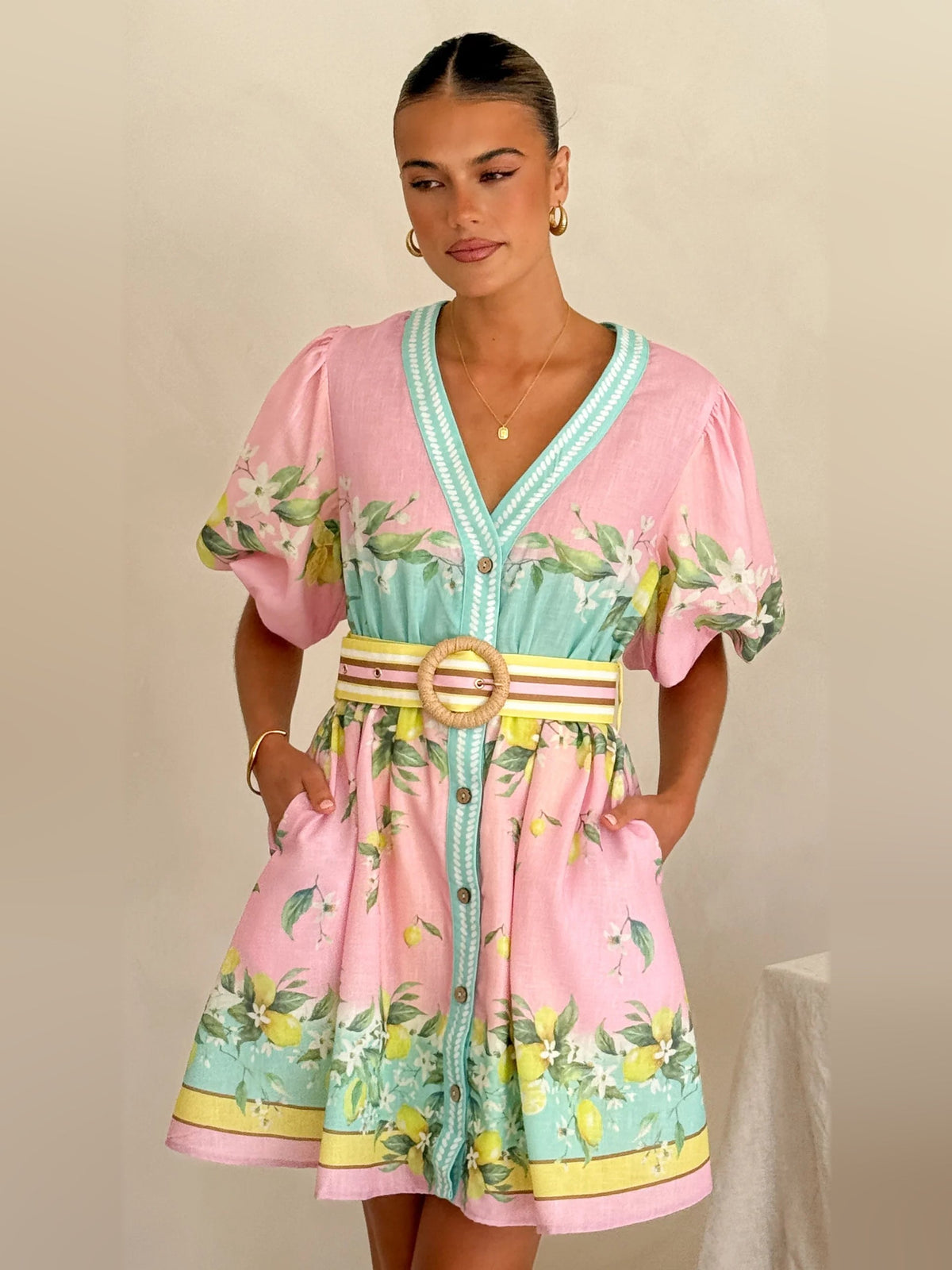 Pink floral mini dress, turquoise V-neck trim and buttons, gold ring belt, puff sleeves.