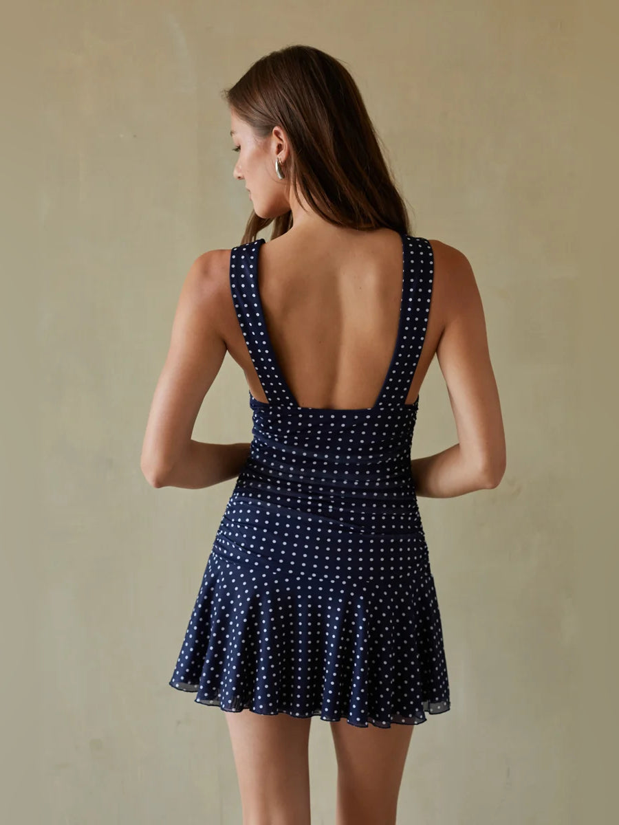 Back view of navy mini dress with open back, sleeveless cut, and white dotted flared skirt