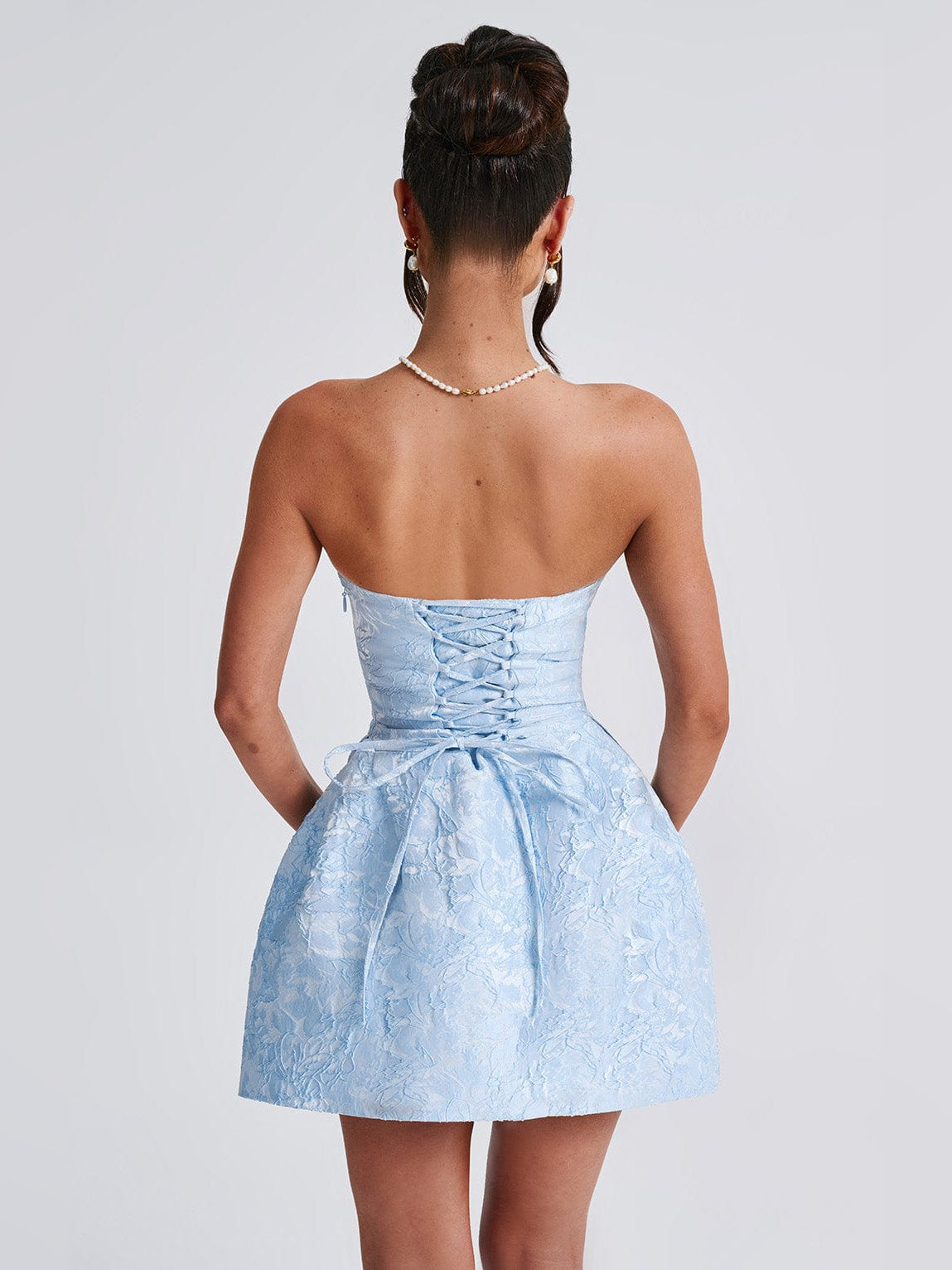 Blue strapless mini dress shown from the back with corset detailing and bow waist.