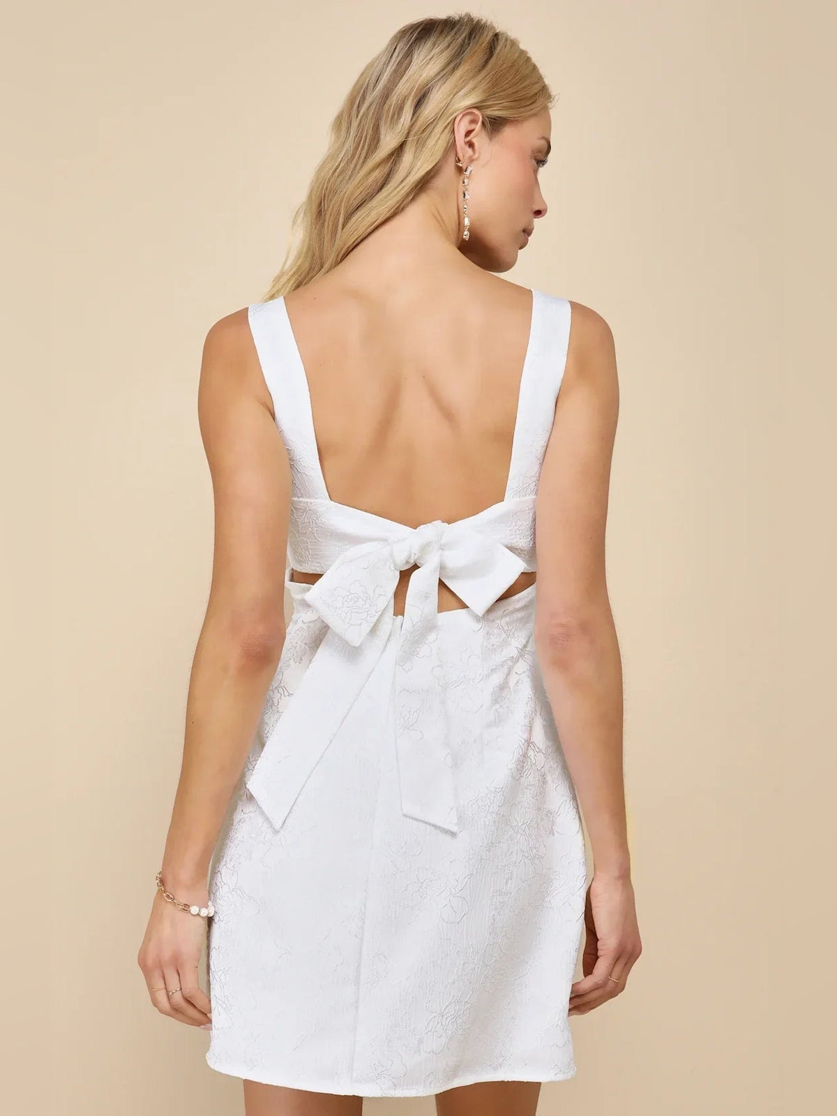 Ivory white mini dress with open back, deep V straps, and bow at lower back