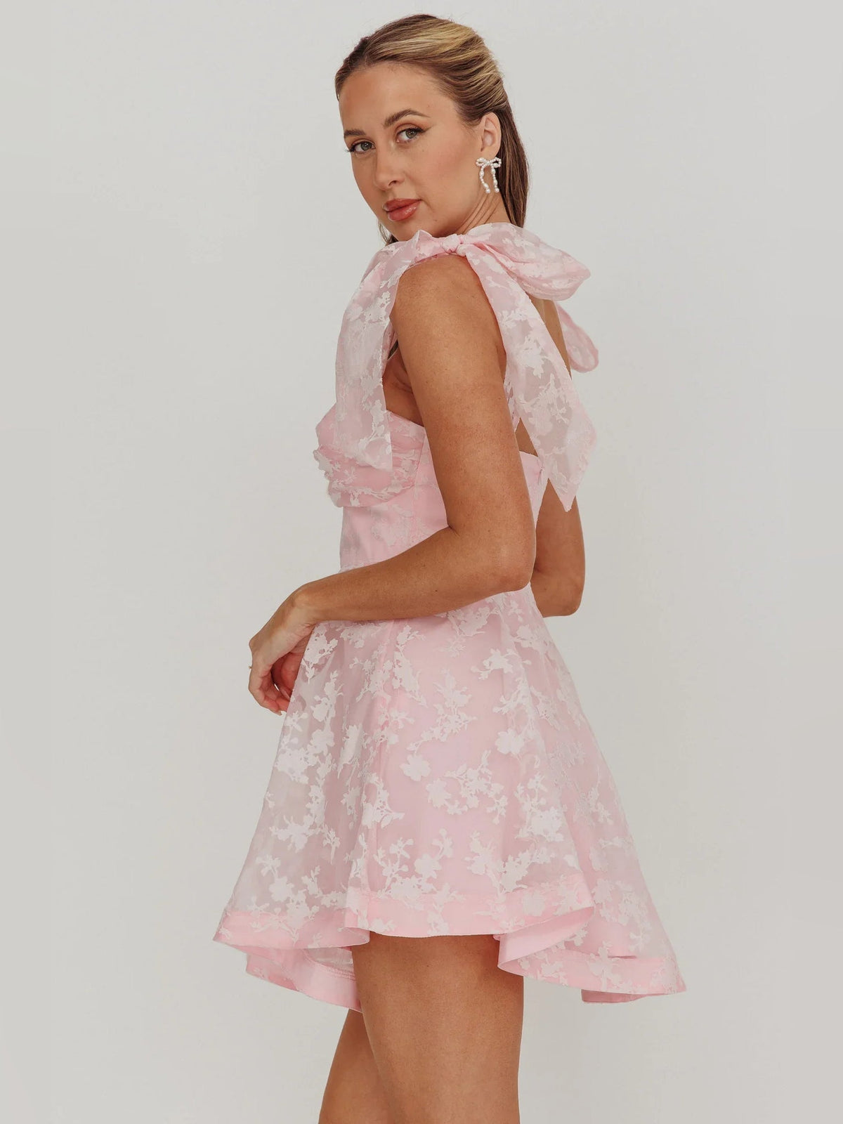 Blush pink mini dress with open back, bow shoulder sleeves, and layered organza floral skirt