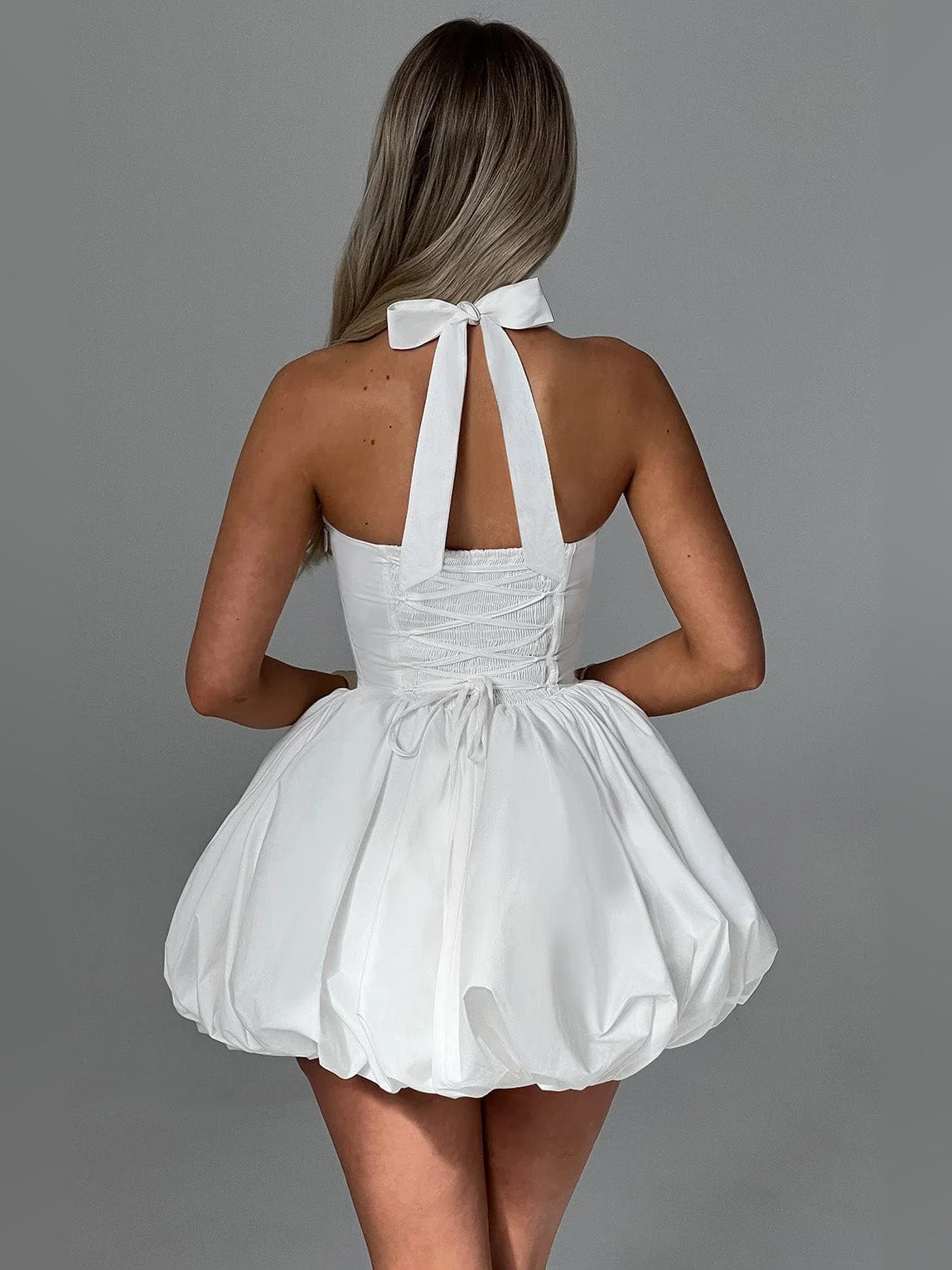 Back view of white corset halter mini dress with bow-tie strap detail and puff skirt