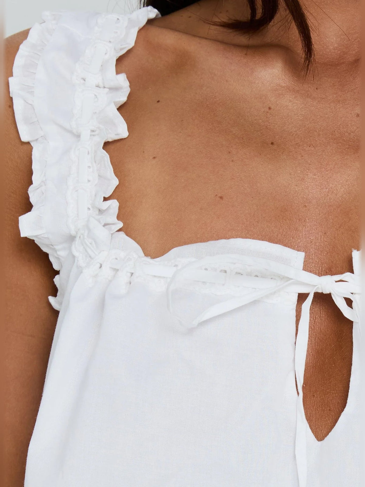 Close-up of white dress neckline with ruffle trim and bow-tie strap detail