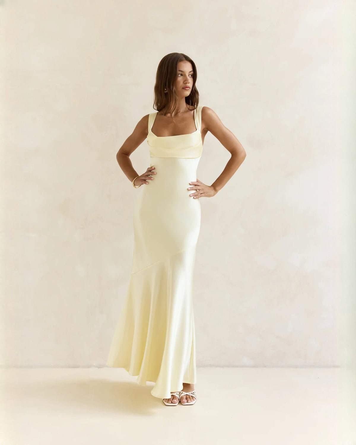 Sleeveless satin A-line maxi dress in pale yellow, hands on hips front view