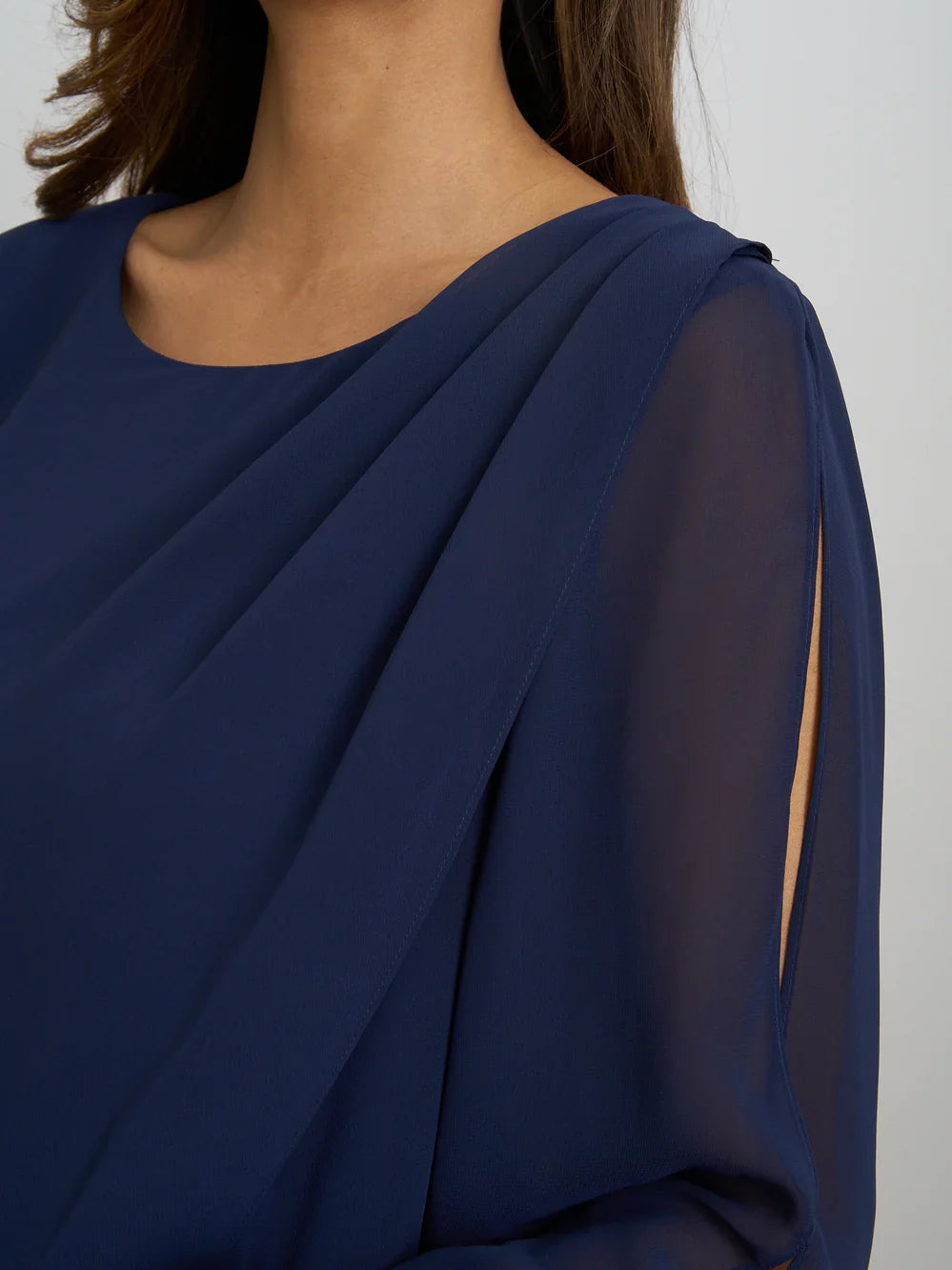 Close-up of dark navy dress neckline with draped chiffon layers and sheer sleeve