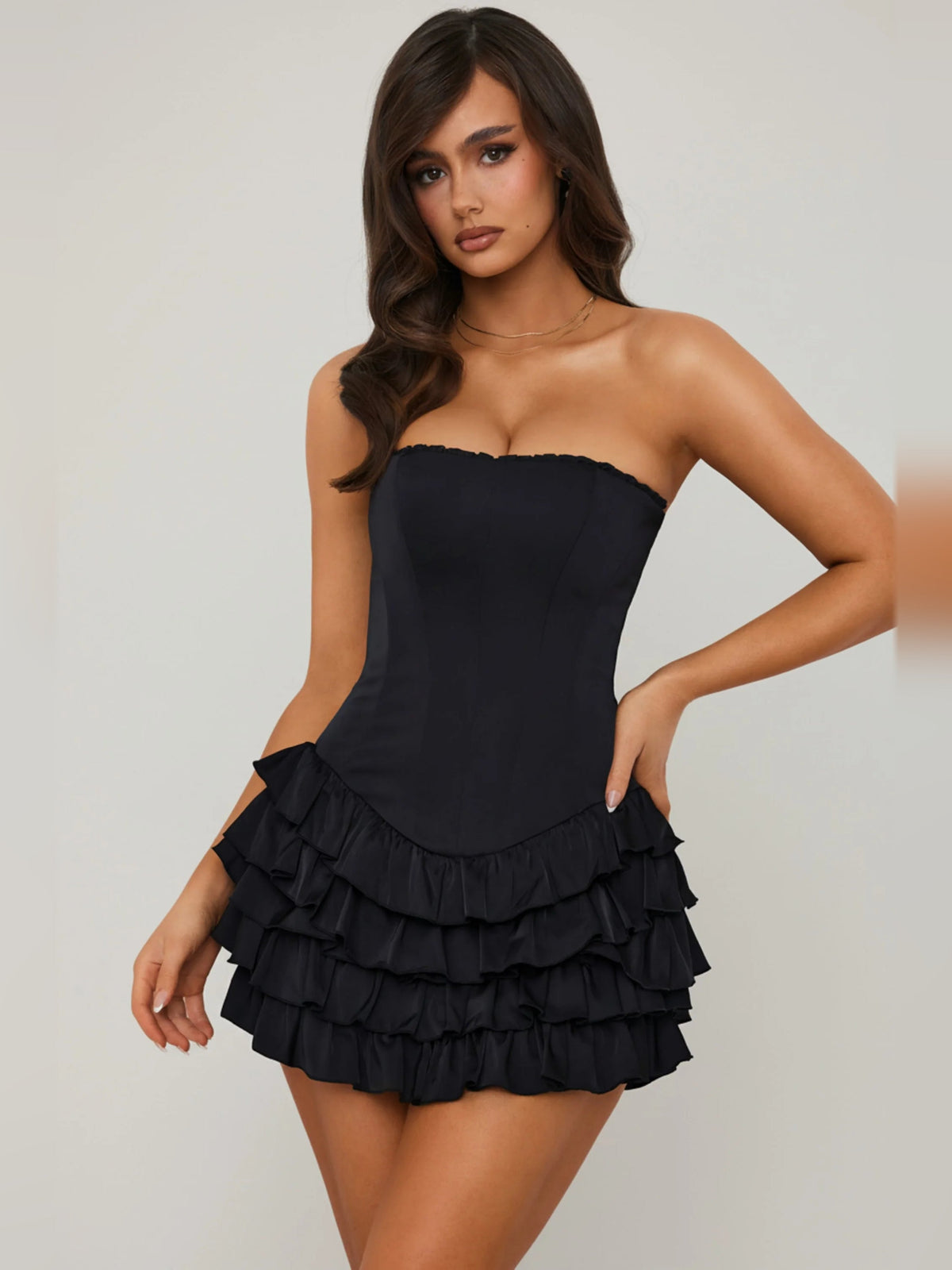 Three-quarter view of black strapless corset mini dress with tiered ruffle skirt.