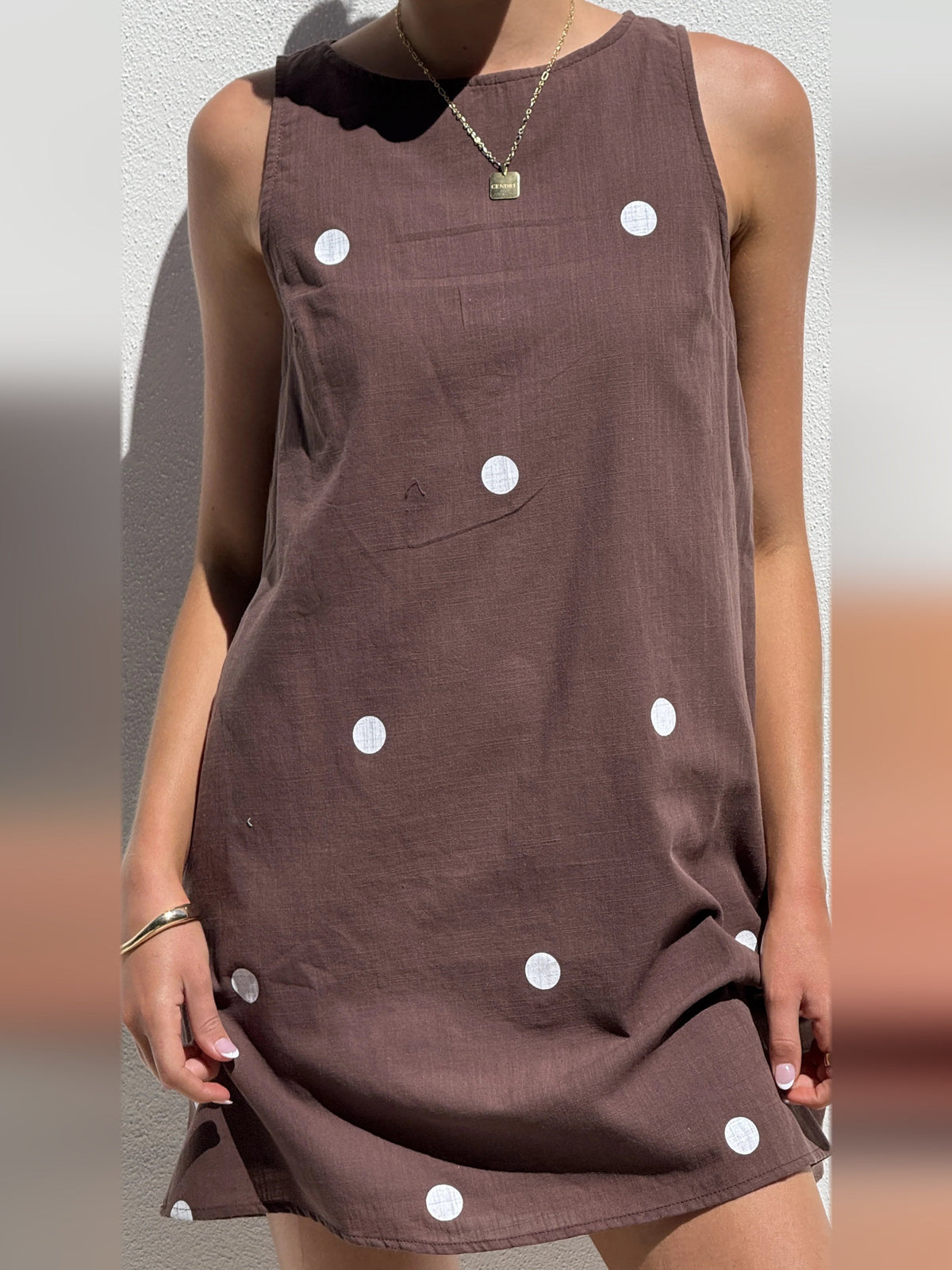 Chocolate-brown sleeveless mini dress with white polka dots; close-up of front