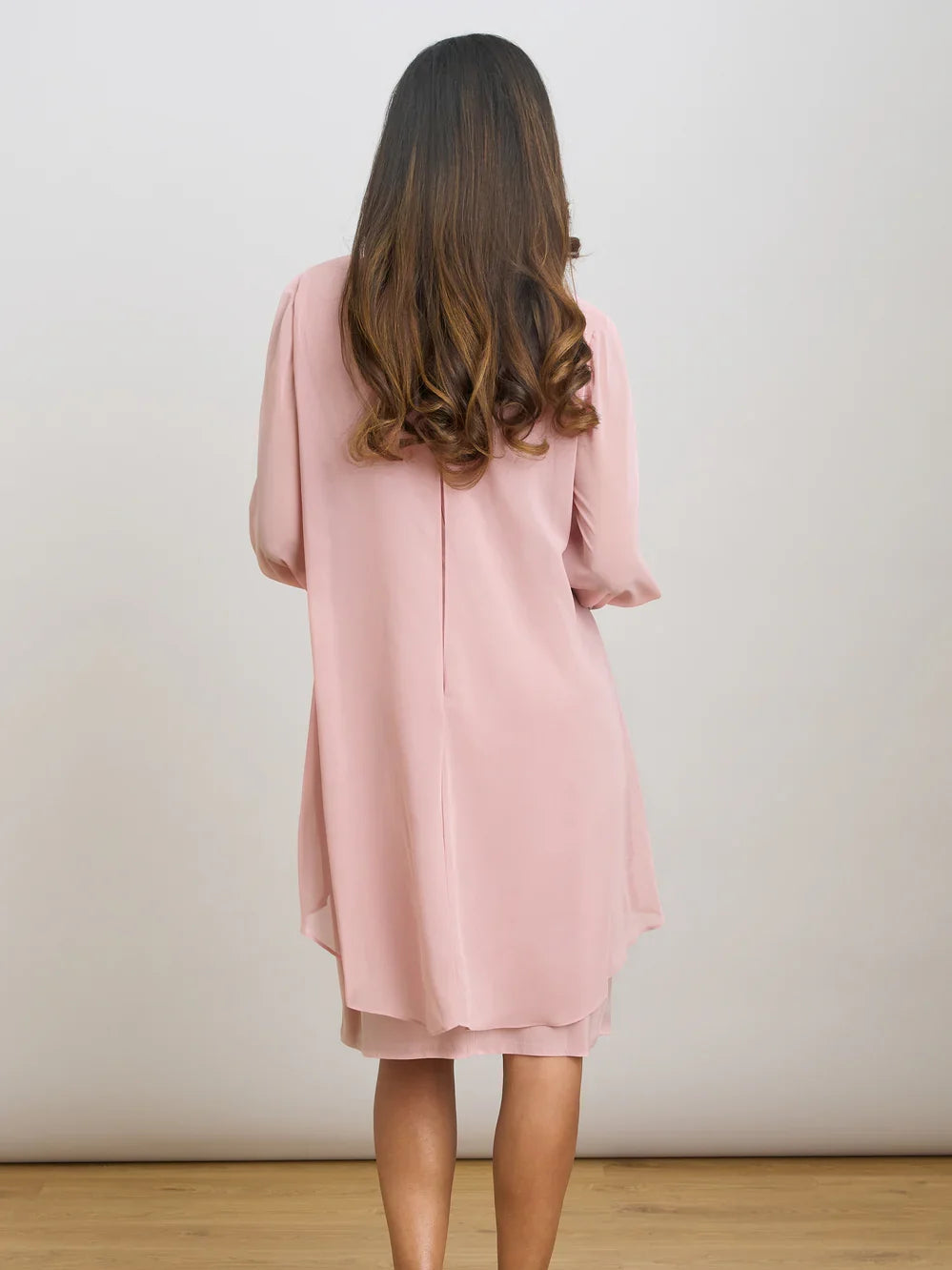 Pink chiffon sheath dress shown from back with draped silhouette and flowing sleeves