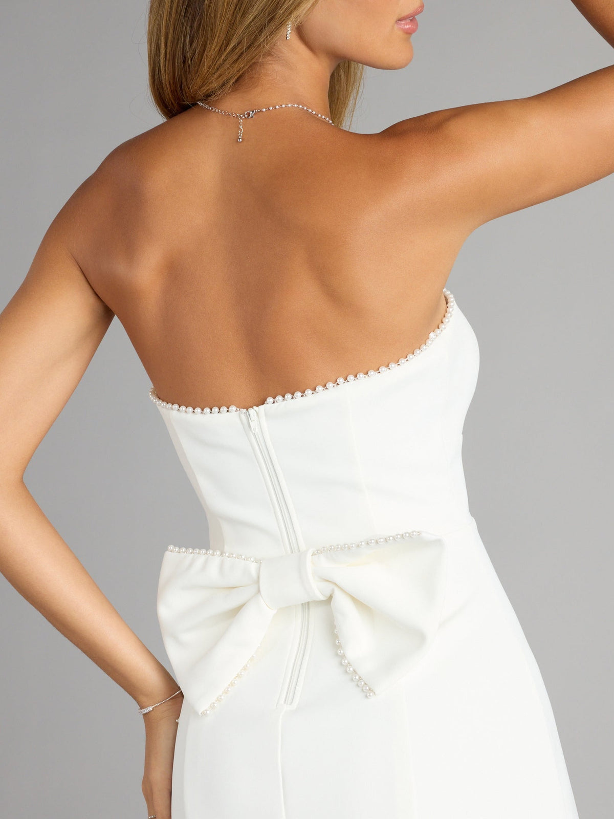 White backless mini dress with scalloped neckline, tied waist bow, and center-back zipper seam