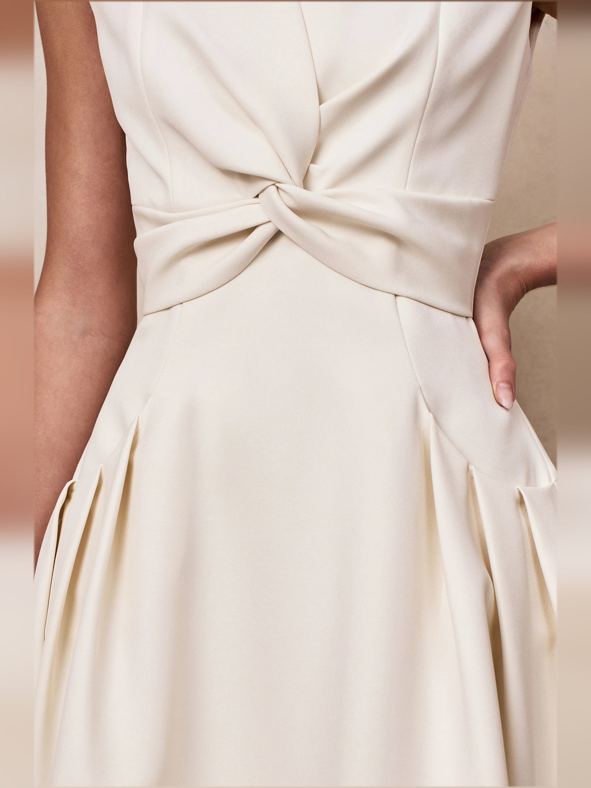 Cream midi dress closeup of twisted knot waist and pleated skirt panel