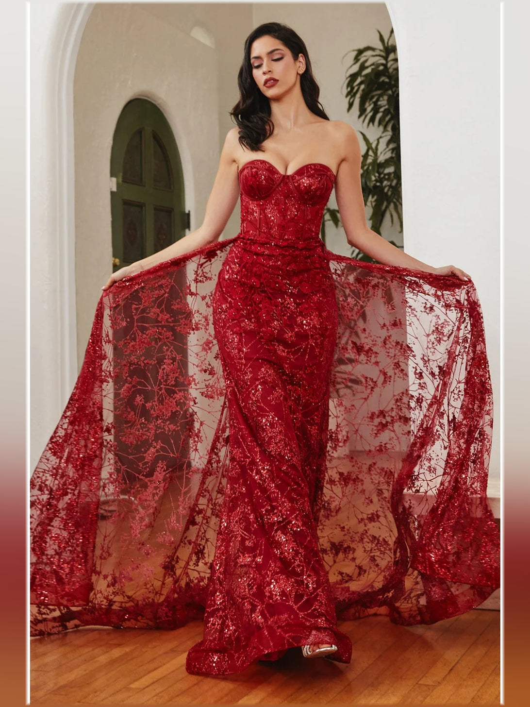 Red mermaid prom dress with corset bodice, sweetheart neckline, and flowing sheer overlay