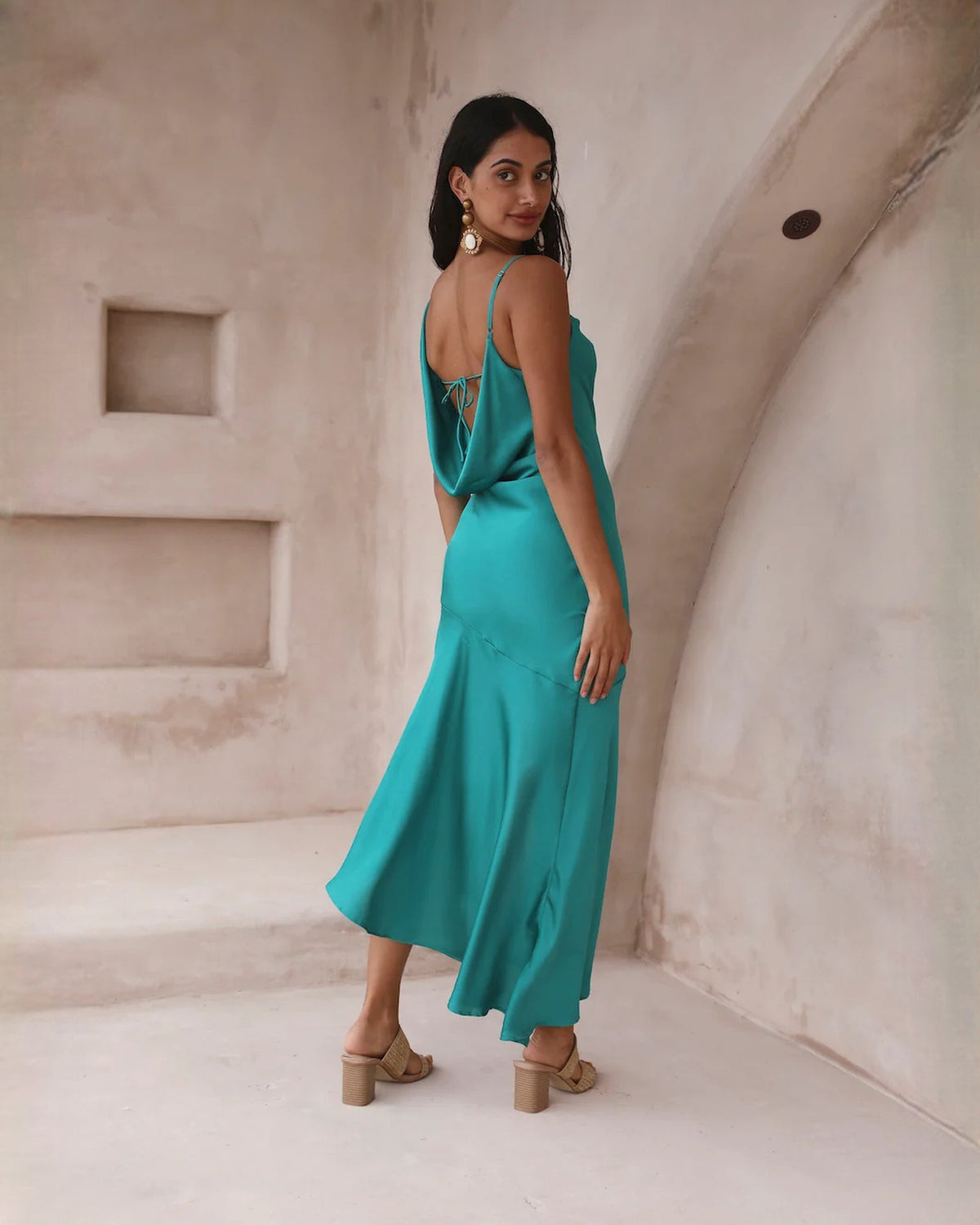 Teal satin sleeveless midi dress with cowl neckline and draped back straps.