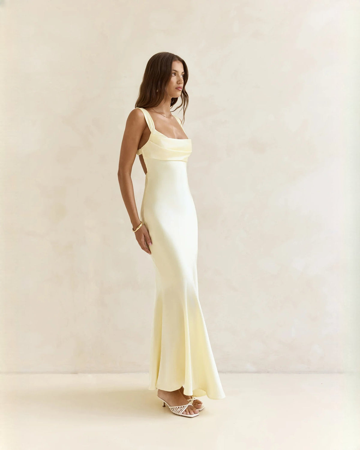 Sleeveless satin A-line maxi dress in pale yellow, angled side view of full skirt