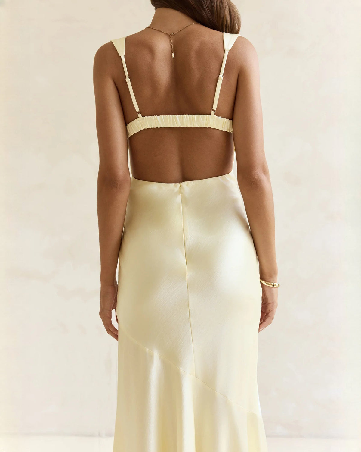 Back view of sleeveless satin A-line maxi dress in pale yellow with open-back straps