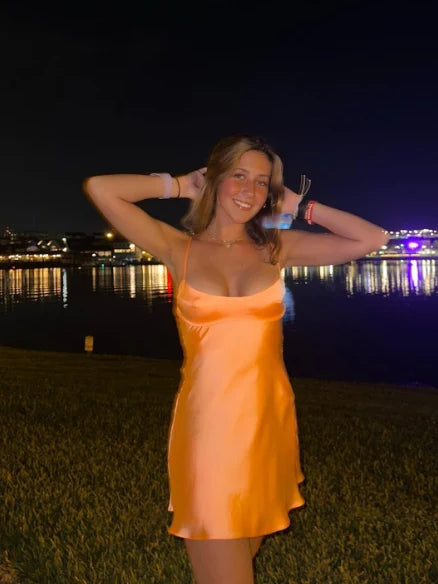 Orange satin mini slip dress with square neckline and spaghetti straps, night outdoor view.