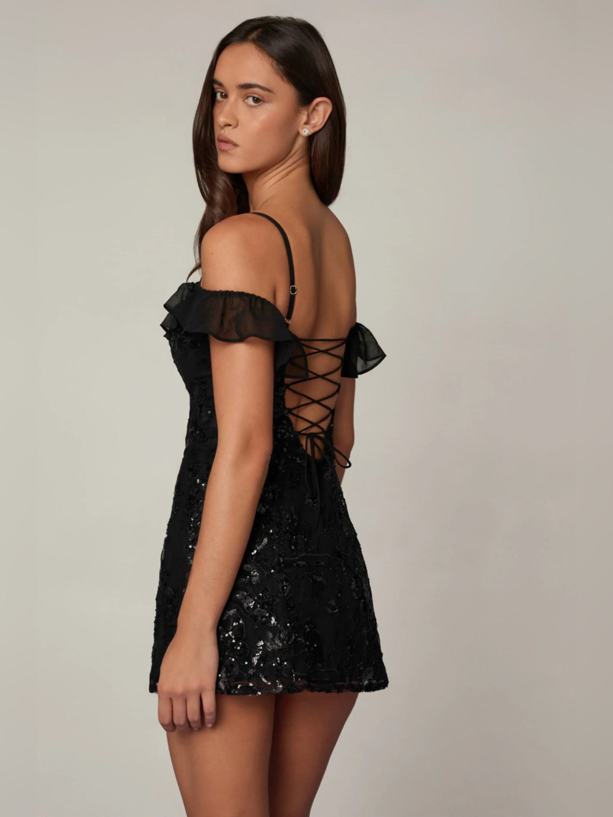Black sequin mini dress side view with off-shoulder ruffle sleeve and crisscross back