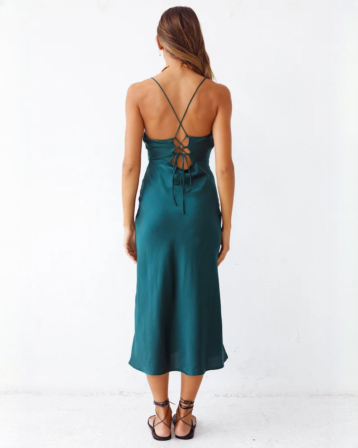 Back view of deep teal satin midi dress with crisscross straps and tied open back
