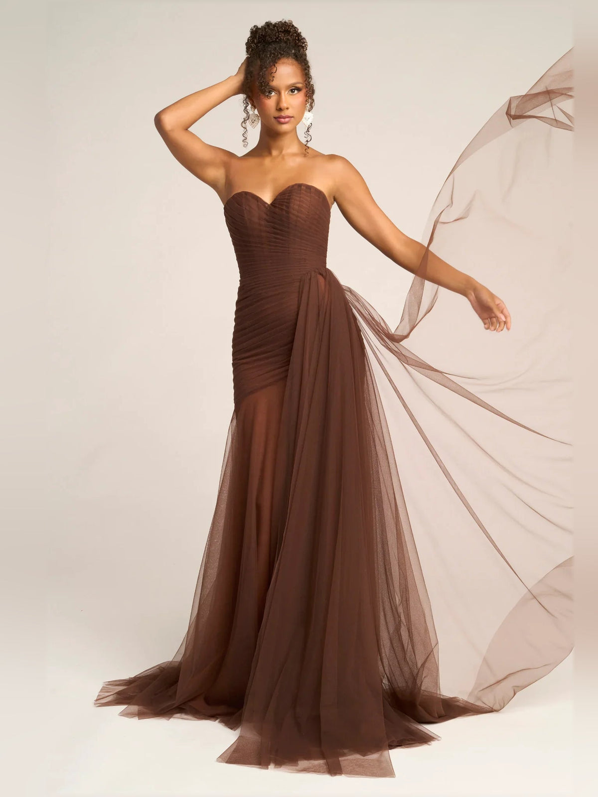 Brown strapless sweetheart draped mermaid formal dress with flowing tulle and train.