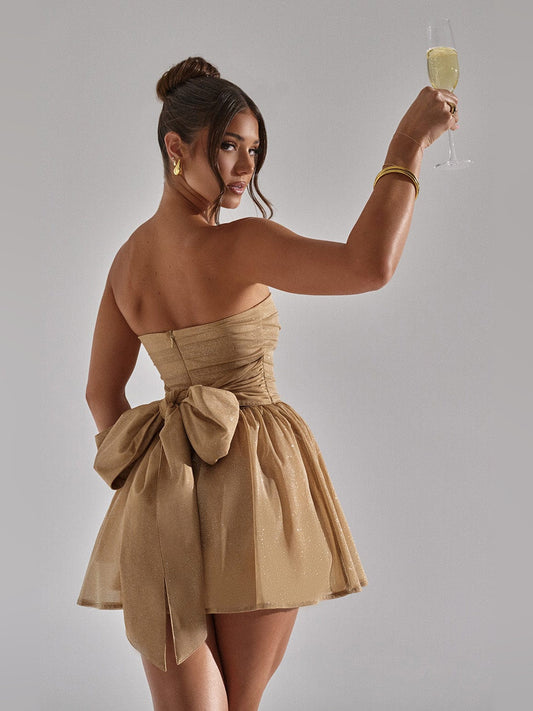 Gold strapless mini dress with large back bow and short flared glitter skirt, angled
