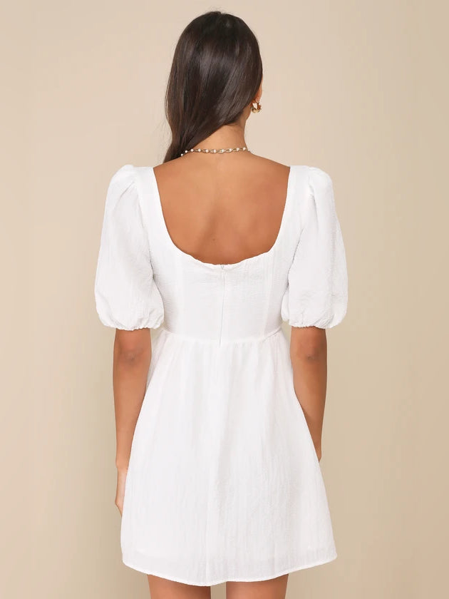 White mini dress with low back scoop and puff sleeves, gathered waist