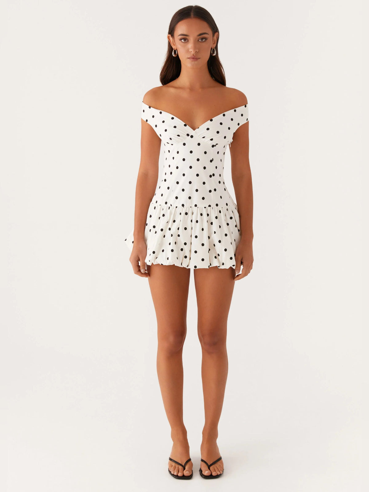Off-shoulder mini dress front view in white with black polka dots, sweetheart neckline, pleated skirt
