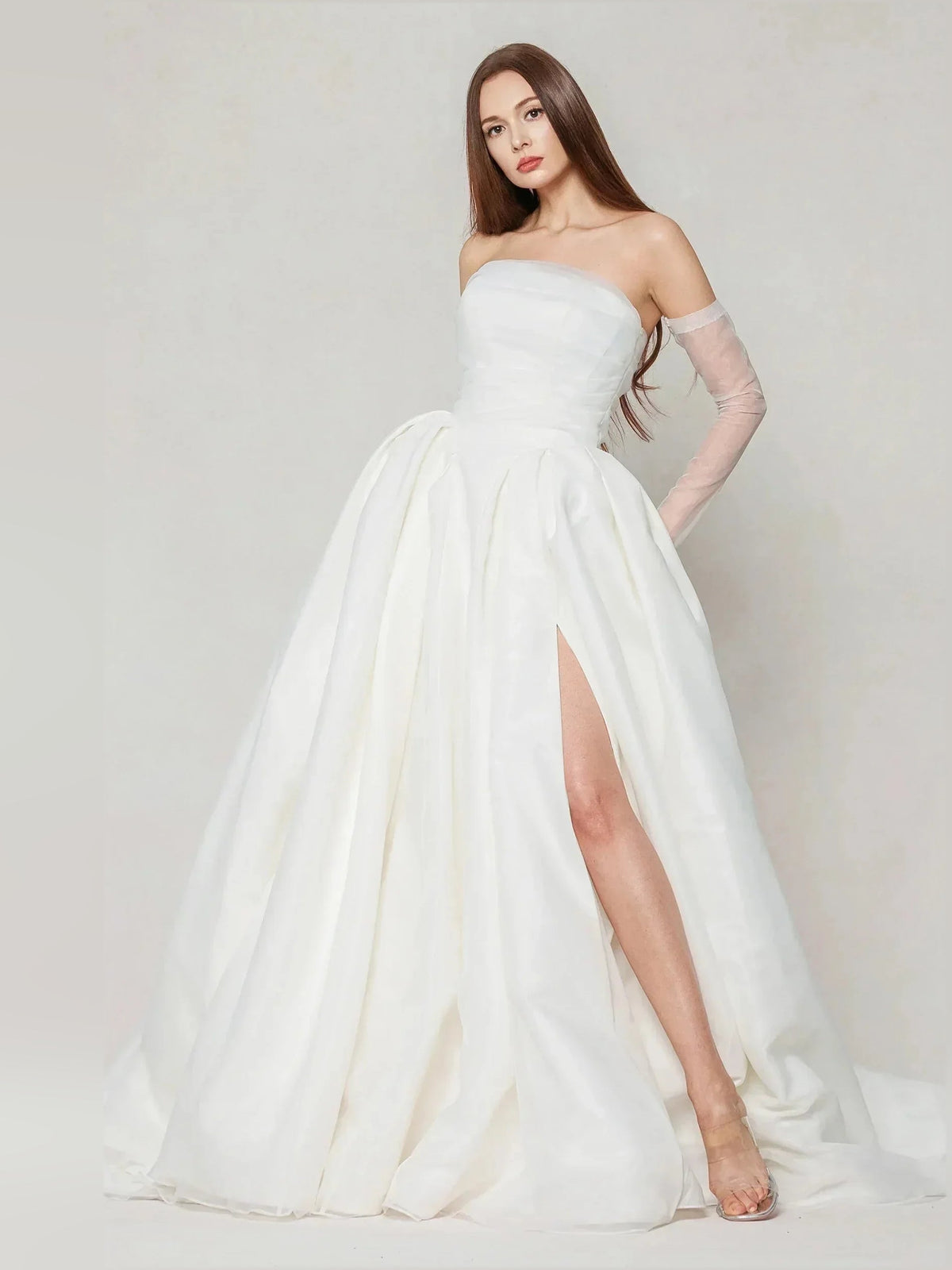 Ivory strapless ball gown featuring pleated skirt and side slit with long, billowy hem