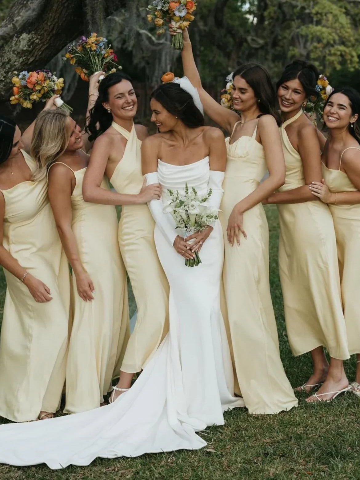 White strapless mermaid wedding dress with long skirt; bride holding bouquet with friends