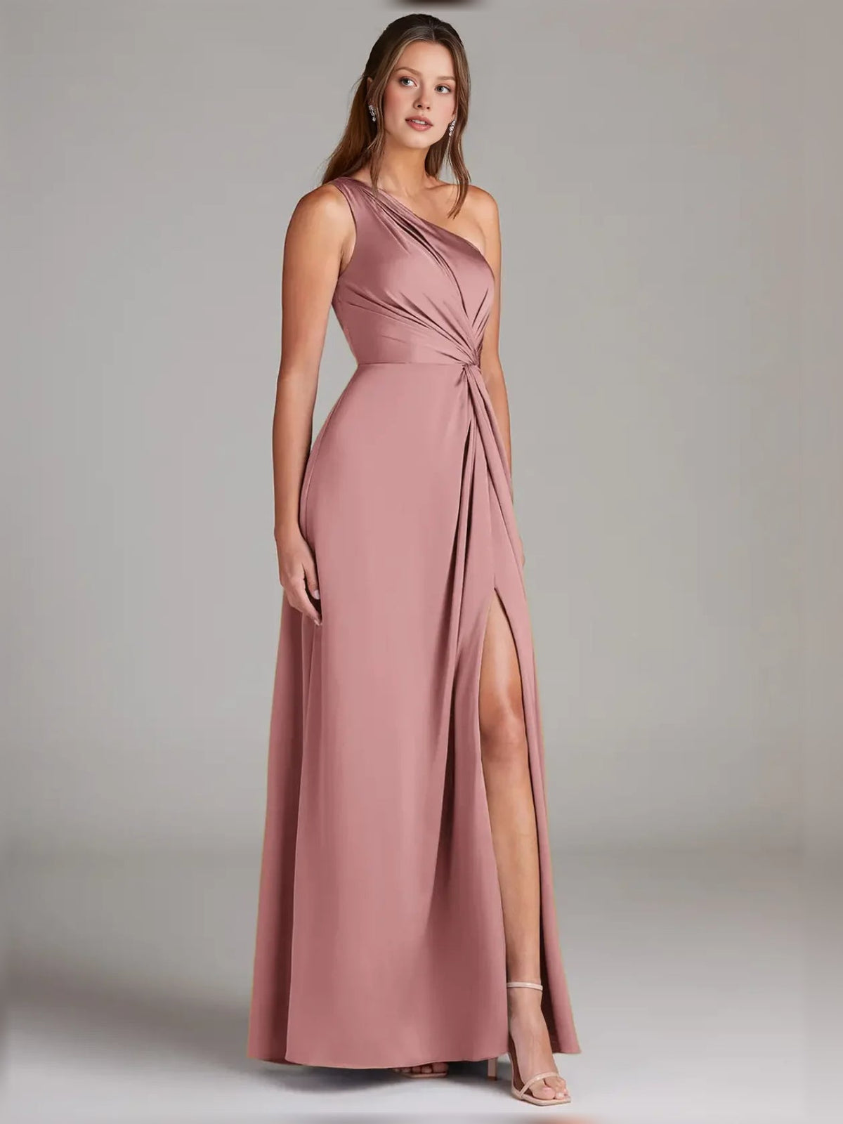 Rose gold one-shoulder formal dress with knot detail and flowing skirt with thigh slit.