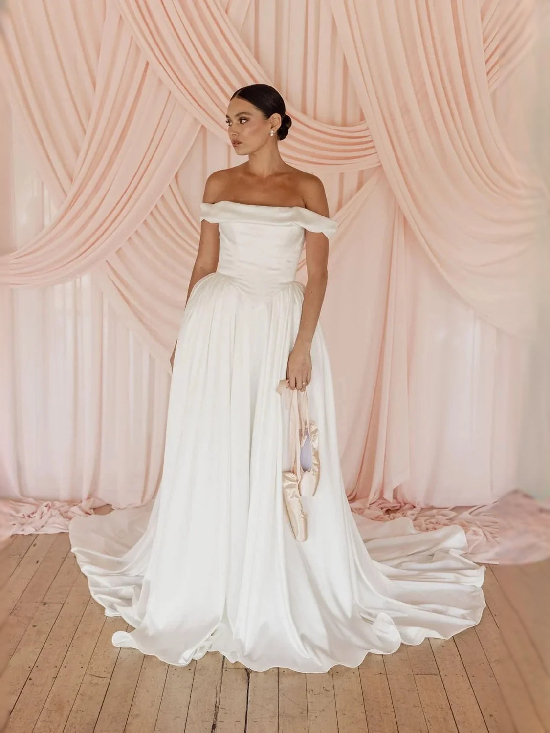 Ivory off-shoulder satin ball-gown wedding dress with pleated skirt and draped bodice
